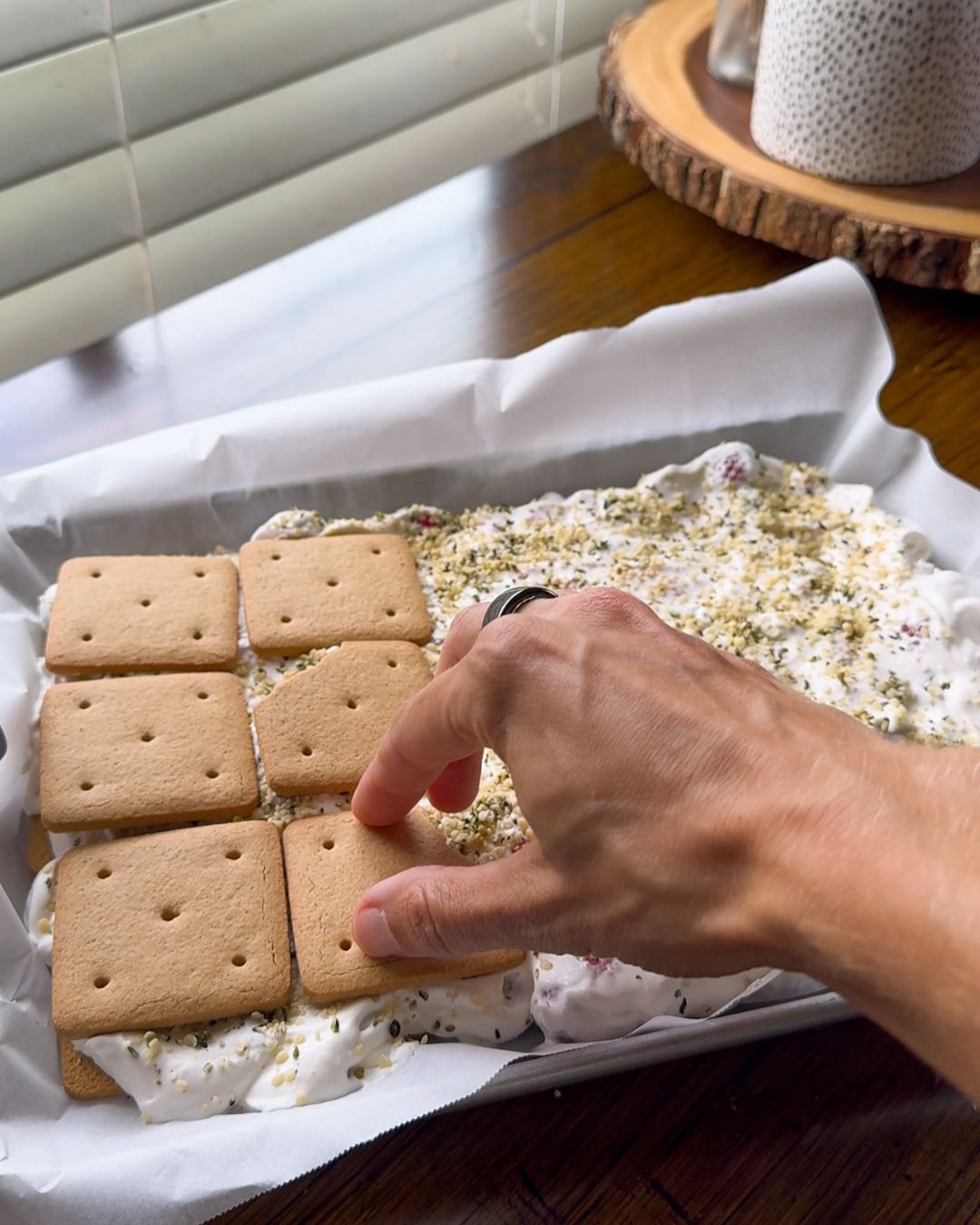 Graham crackers being layered with Greek yogurt, whipped cream, and berries before freezing into sandwich snacks