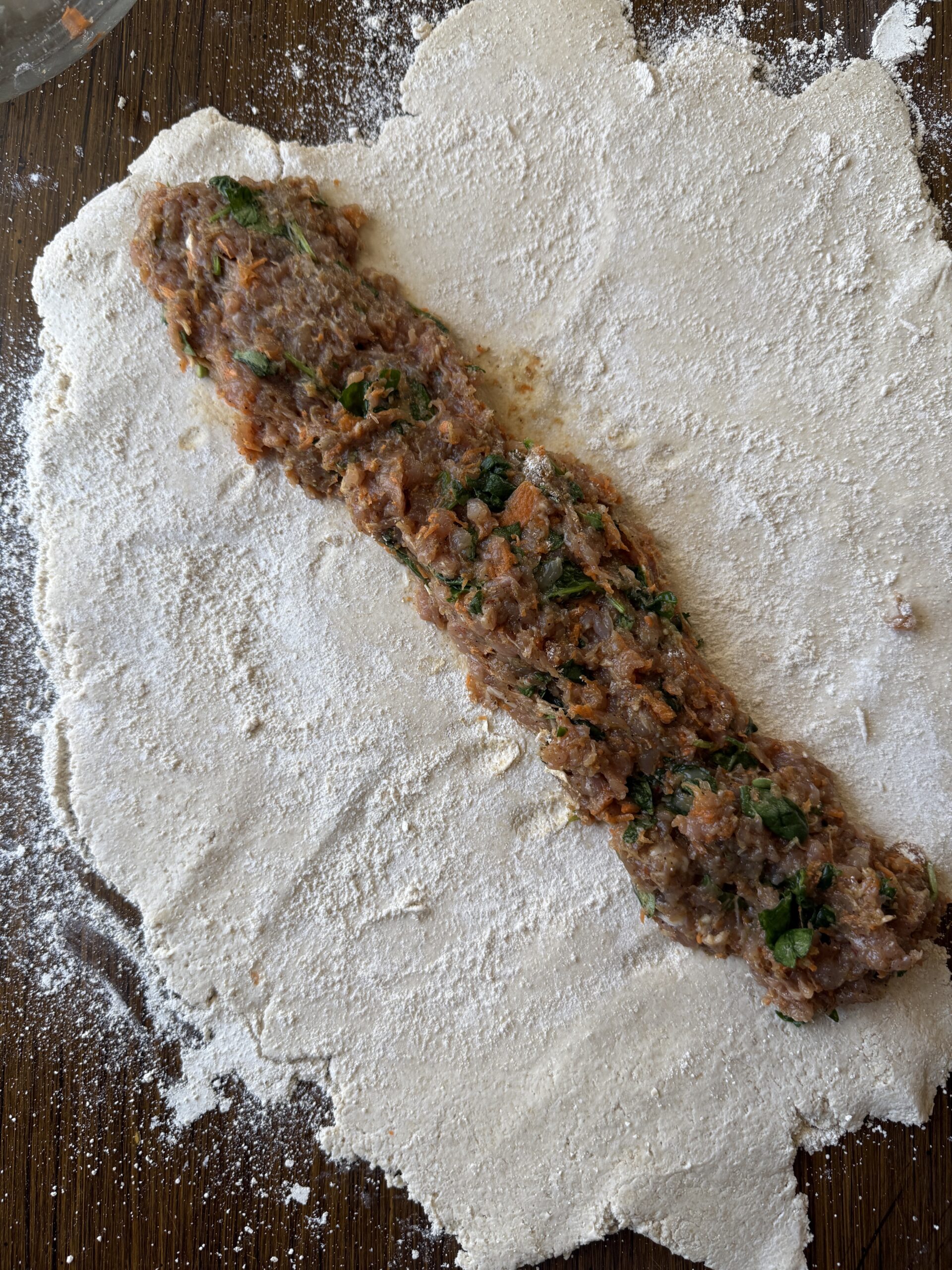 rolling out the sausage mixture onto the yogurt dough mixture to wrap into sausage rolls
