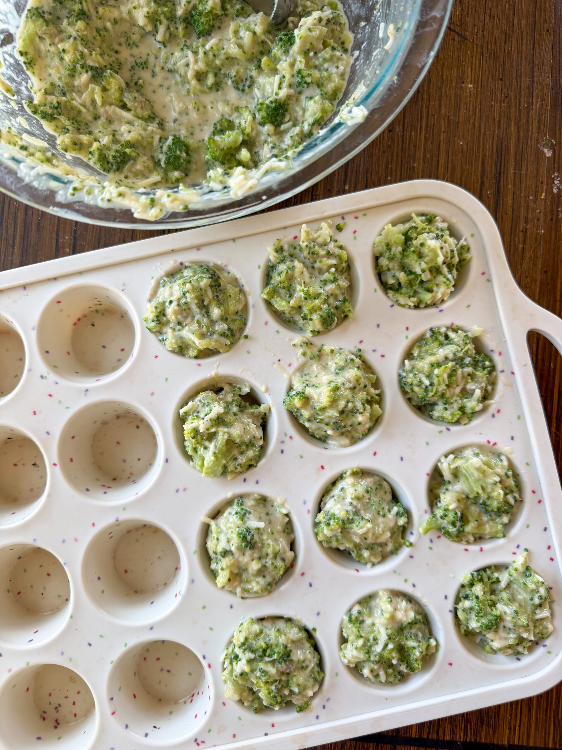 scooping broccoli cheese mini muffin mixtures into muffin pan